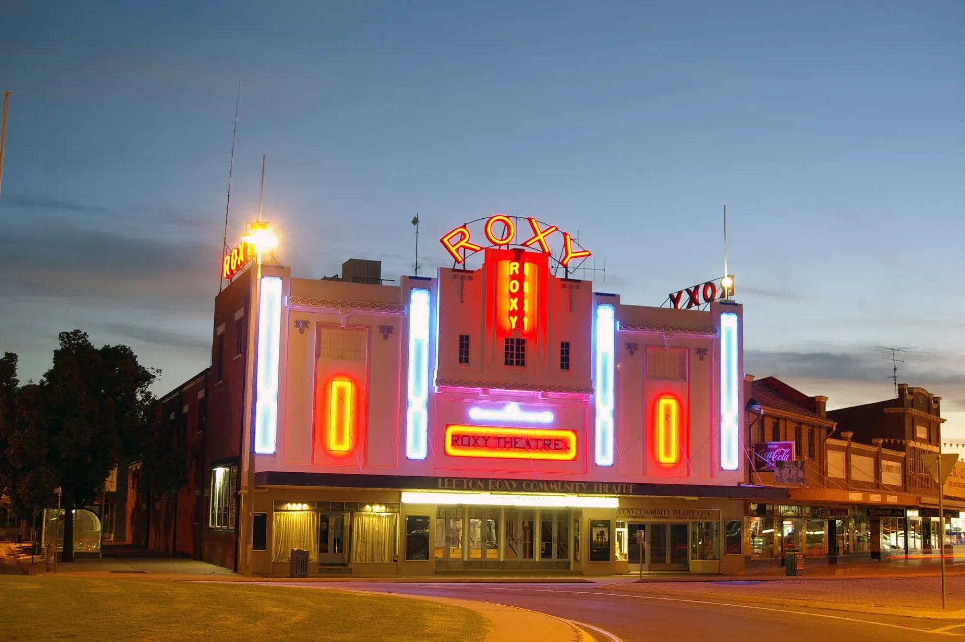 The Roxy Community Theatre at dusk — heritage-listed Art Deco facade with illuminated neon ROXY sign on Pine Avenue Leeton